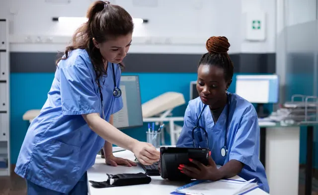 两名身着蓝色工作服的医疗助理正在查看平板电脑上的病人病历