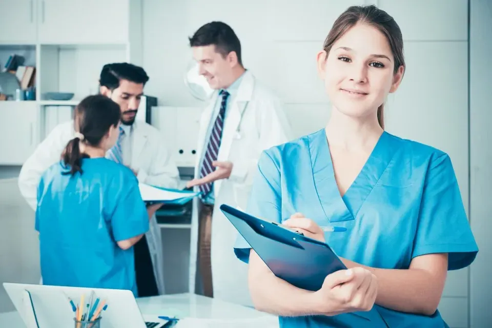 Smiling Medical Assistant with Clipboard with Doctors in Background