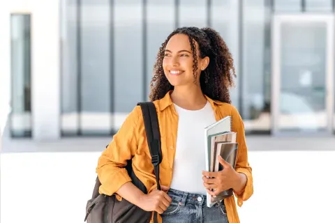 Student wearing backpack and smiling holding textbook